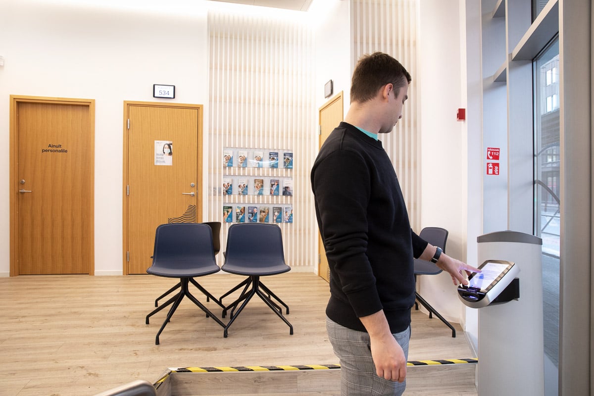 Person taking a ticket at a kiosk inside Synlab